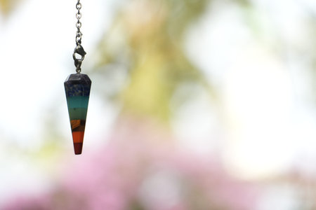 A colorful seven chakra healing pendulum hangs vibrantly against a soft, bright background.