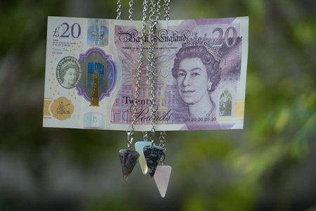 A twenty pound sterling note hangs elegantly with multiple crystal pendulums.