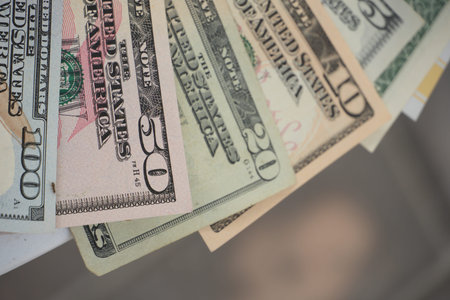 A neatly fanned stack of US dollar bills is displayed against a textured gray background.