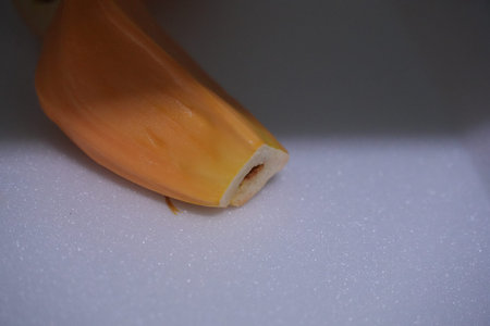 The tip of a partially peeled yellow banana or plantain rests on a white surface.