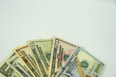 A close-up shows United States dollar bills fanned out on a simple white surface.