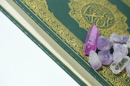 A vibrant purple crystal and small raw stones accompany an elegantly designed Holy Quran.