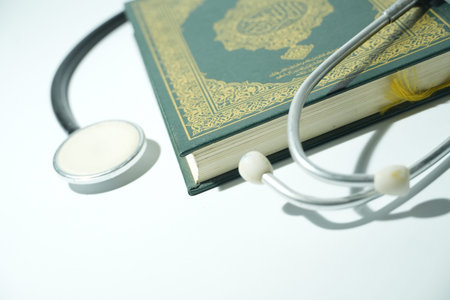 A stethoscope rests beside an ornate green Holy Quran on a clean white background.の写真素材