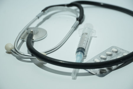 A stethoscope, syringe, and pill blister pack are displayed on a crisp white medical background.