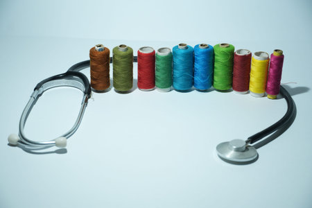 A medical stethoscope curves around a vibrant line of colorful sewing thread spools.の写真素材