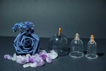 A blue fabric rose, healing crystals, and cupping therapy cups are arranged together on a dark...