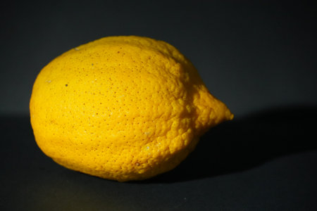 A textured yellow lemon with a unique pointed end casts a shadow on the dark background.