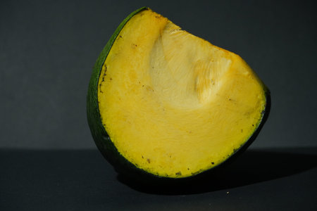 A freshly cut half of a green mango, revealing its bright yellow flesh on a dark surface.