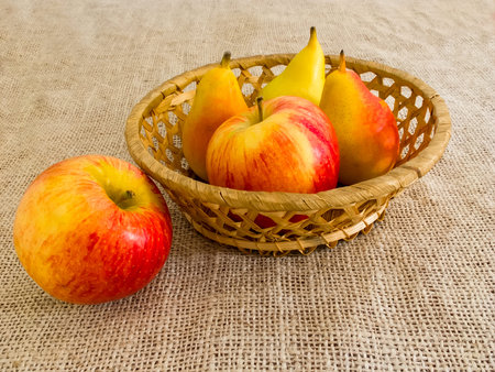 Fresh red apples and pears in a straw basket on canvas.の写真素材