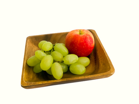 Apple and grapes on a wooden plate isolated on white backgroundの写真素材