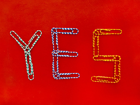Word yes laid out from paper clips against red backgroundの写真素材