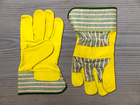 Two new yellow leather work gloves lying on wooden board. Top view.の写真素材