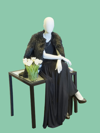 Sitting female mannequin wearing black evening dress and fur cape, isolated.  No brand names or copyright objects.の写真素材