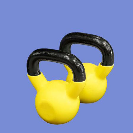 Two yellow kettlebells isolated on blue background. Weights for fitness training.の写真素材