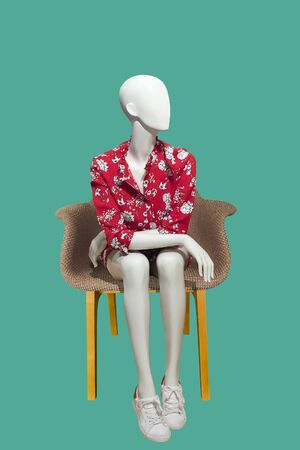Sitting female mannequin wearing fashionable red dress, isolated on green background.  No brand names or copyright objects.の写真素材