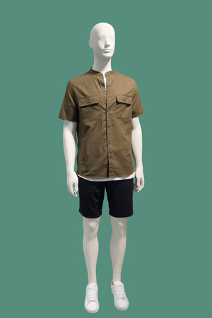 Full-length male mannequin dressed in brown short sleeve button-down shirt and black shorts, isolated on green background. No brand names or copyright objects.の写真素材