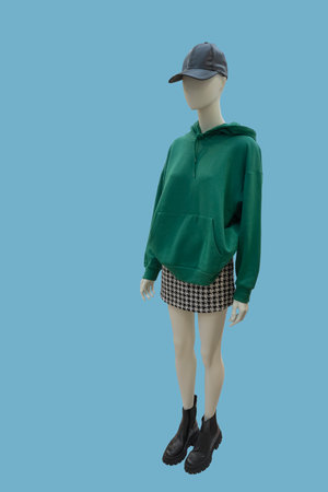 Full length image of a female display mannequin wearing green kangaroo pocket hoodie and plaid tweed skirt isolated on blue backgroundの写真素材