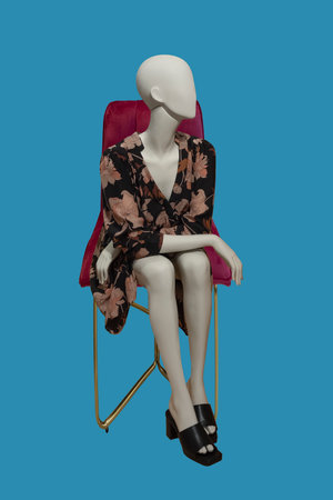 Sitting image of a female display mannequin wearing fashionable clothes isolated on blue backgroundの写真素材