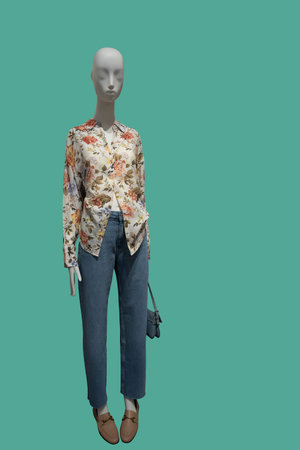 Full length image of a female display mannequin wearing long sleeve blouse with floral pattern and blue jeans over green backgroundの写真素材