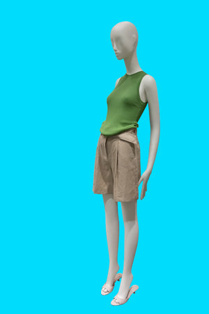 Full length image of a female display mannequin wearing green sleeveless t-shirt and light brown shorts isolated on blue backgroundの写真素材