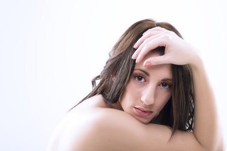 Serious pensive attractive woman with bare shoulders and tousled long brunette hair looking directly at the camera in studioの写真素材
