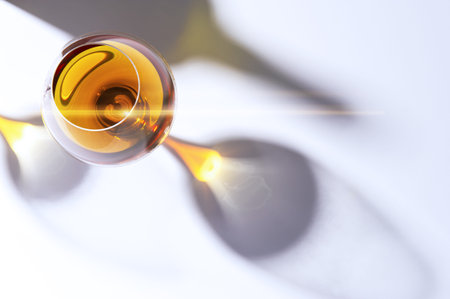 Overhead view of glowing amber cognac in a snifter casting a shadow over a white background together...