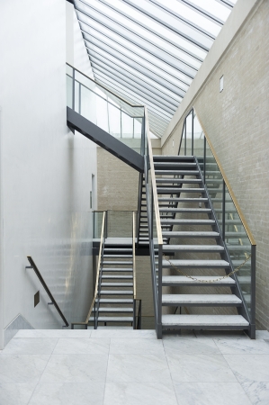 Modern interior staircase with a steel frame, open treads and a transparent glass bannister on multiple levels under a glass skylight ceilingのeditorial素材