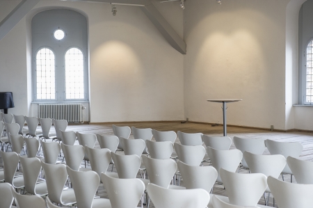Modern white modular seating arranged in rows in a bright airy lecture hall, view from behind facing a small circular podium or tableのeditorial素材