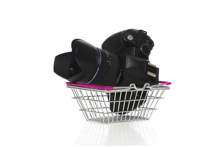 Modern dslr camera, lens and lenshood in a metal shopping basket on a white background conceptual of retail, consumerism and purchasingの写真素材