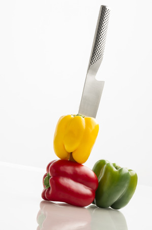 Three colourful sweet bell peppers in yellow, green and red pierced with a stylish stainless steel kitchen knife の写真素材