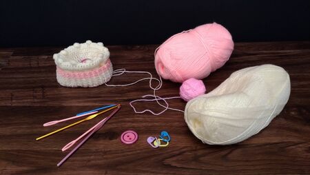 Crocheted hat with colorful yarn balls and crocheting accessories, hooks, needles and buttons on a wooden tableの写真素材