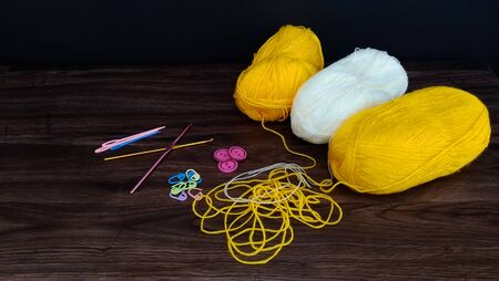 knitting white and yellow balls with crocheting accessories .crocheting accessories are hooks,needles and buttons on a wooden table.close up shotの写真素材