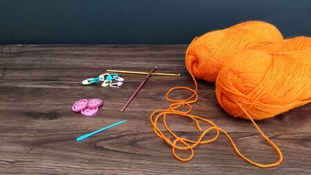 Close up shot of orange yarn balls for crochet with crocheting accessories on wooden tableの写真素材