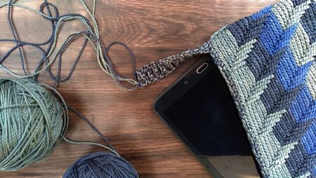 crocheted bag for digital tablet and blue yarn balls on wooden background.top view,close up shotの写真素材