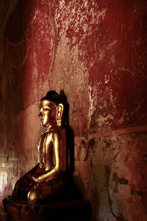 Golden buddha statue in the front of a weathered painted wall at an old buddhist temple in Bagan, Myanmar / Burma.の写真素材
