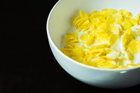 cornflakes in bowl on black table with milk in morningの写真素材