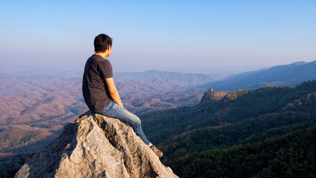 man sitting on stone top of high mountainの写真素材