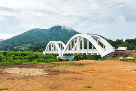 old white railway bridge and mountain in background with overcast sky lamphun thailandの写真素材