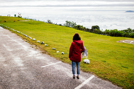 woman wear red coat looking fog and misty on mountain in sunrise timeの写真素材