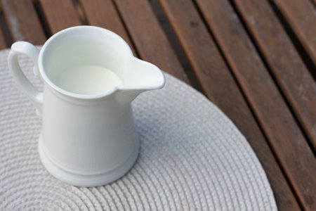 White jug with milk on a wooden table. Breakfast on the veranda. Fresh drink, autumn leaves and oudoor. close up photographyの写真素材