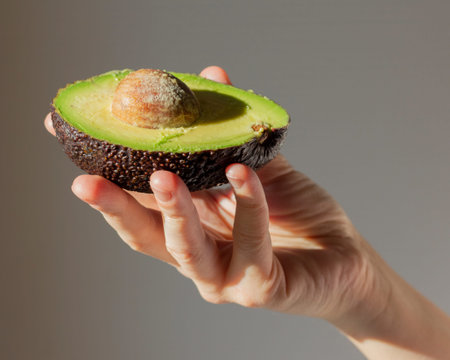 Avocado in a woman hand. green ripe fruit. Sliced half with pulp. Healthy diet food. Culinary...