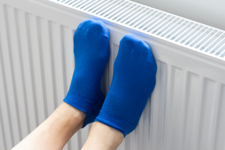 A woman warms her feet in woolen socks on a radiator. home heating. Low temperature and cold in the house. photo closeupの写真素材