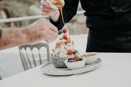 A man decorates a cup of coffee with ice cream and berries.の写真素材