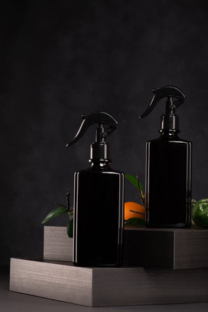 Set of black cosmetic bottles with pump dispenser and green leaves on dark background