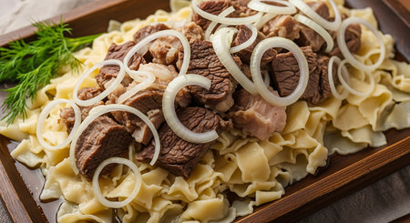 A close-up view of a traditional Beshbarmak meal, showcasing succulent meat, wide pasta, and fresh onion rings on a wooden platter.の素材