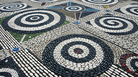 High-detail stone mosaic artwork depicting an owl's face using concentric circles and pebble patterns, set in a spacious courtyard with geometric floor designs and architectural elements.の素材