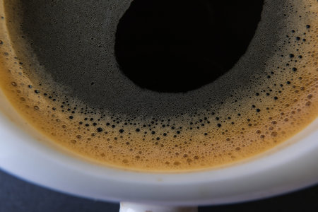 Coffee cup with foam on black background, top view.