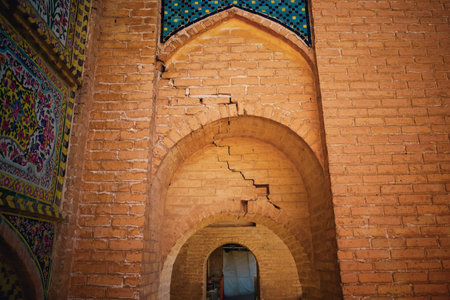 A close-up view of a brick wall featuring a cracked archway. The wall is adorned with colorful tiles...