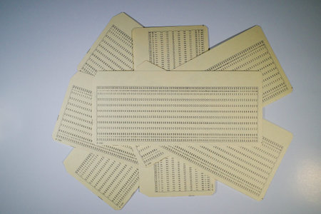A collection of vintage punch cards arranged in a fan shape, showcasing rows of holes representing...