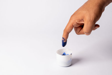 A hand with a finger dipped in blue paint, touching a small white container of paintの写真素材